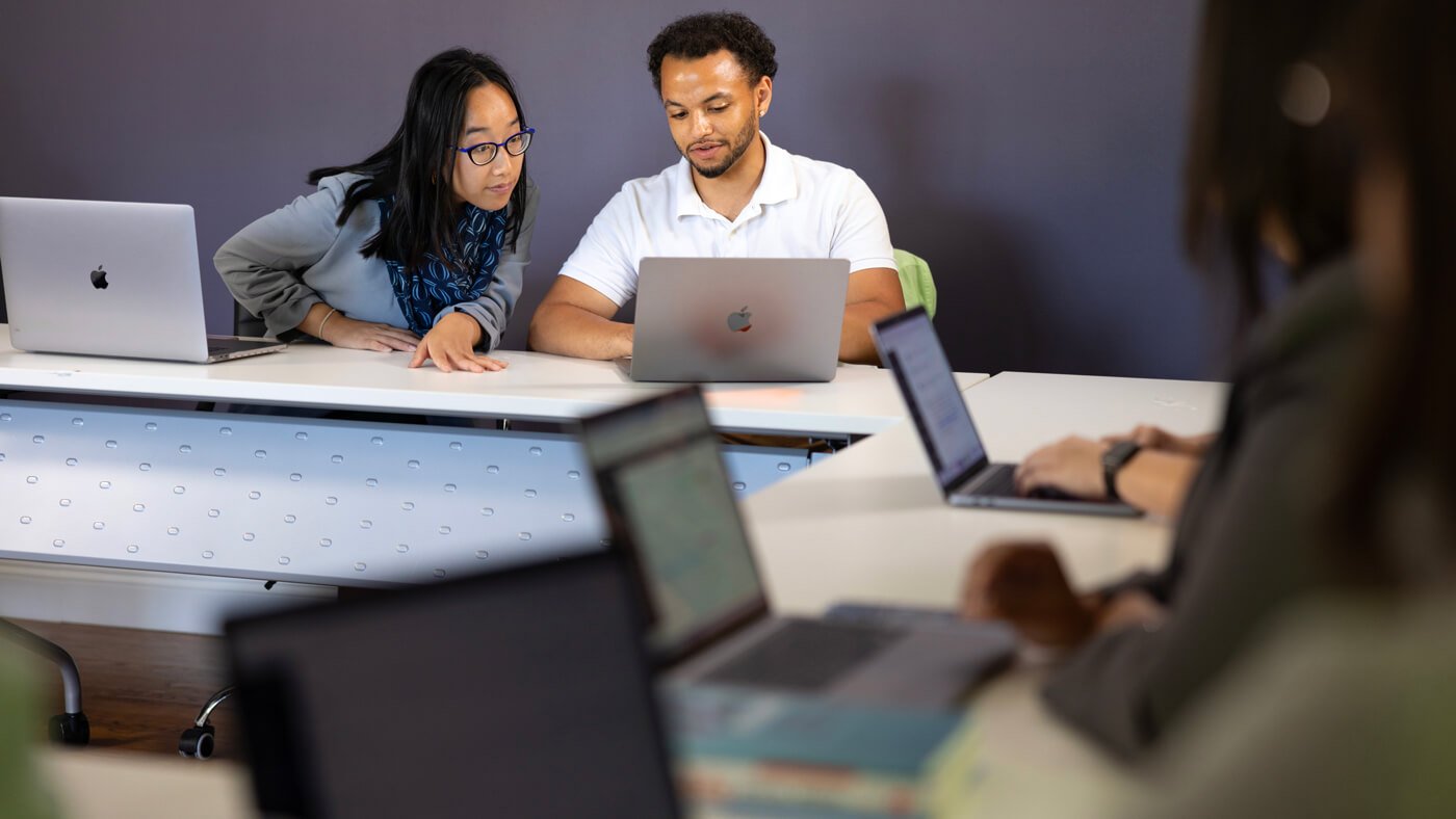 Two students collaborating on a laptop in a classroom setting.