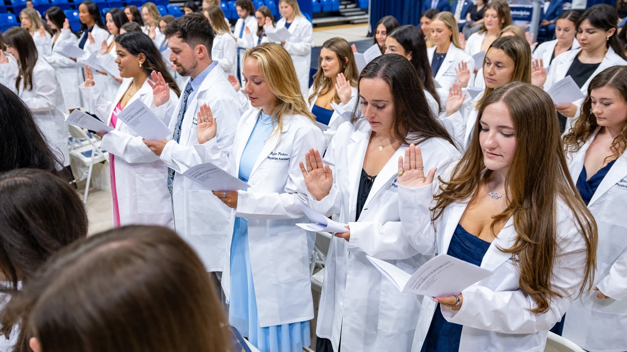 Dozens of Quinnipiac physician assistants in their white coats hold up their hands to say an oath